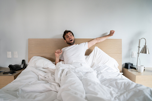 Lazy man waking up in the morning and yawning in bed â lifestyle concepts