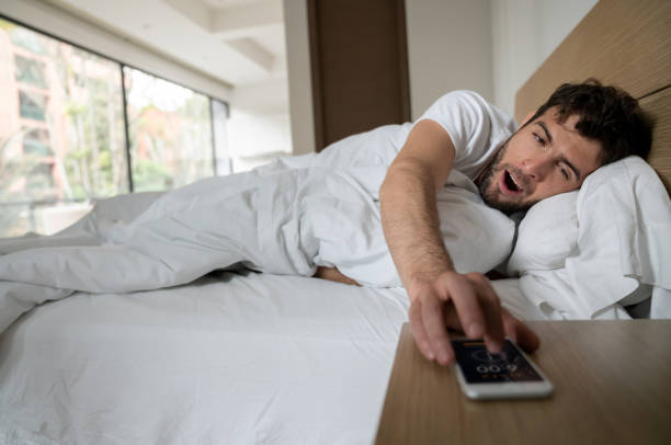 istock Lazy man in bed snoozing the alarm 1209669684