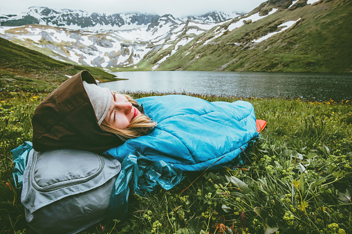 Woman relaxing in sleeping bag laying on grass enjoying lake and mountains landscape Travel Lifestyle camping concept adventure summer vacations outdoor harmony with nature