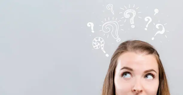 Question marks with young woman looking upwards on a gray background