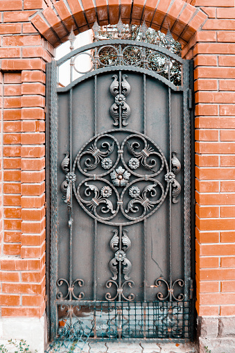 Metal forged front door with a beautiful openwork pattern in the brick wall on the street. The vertical frame.