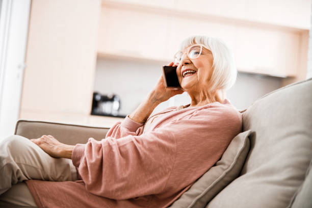 Cheerful old woman talking on cellphone at home