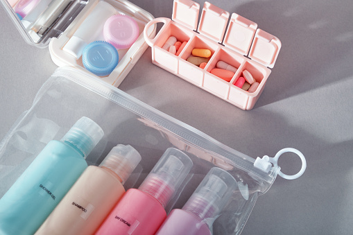 Travel kit. Set of four small plastic bottles for cosmetic products in transparent bag, kit for contact lenses, pill organizer. Gray background with shadows.