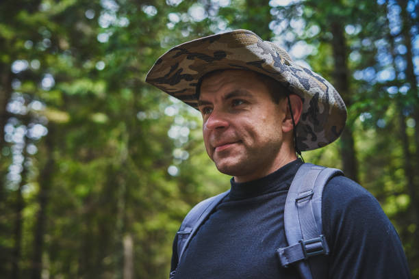 istock Young forester in traditional and folklore coat and hat with feather walking through the forest - back view. Photo from behind - Illuminated man with hat in green forest with foliage - dark portrait. 1209682103