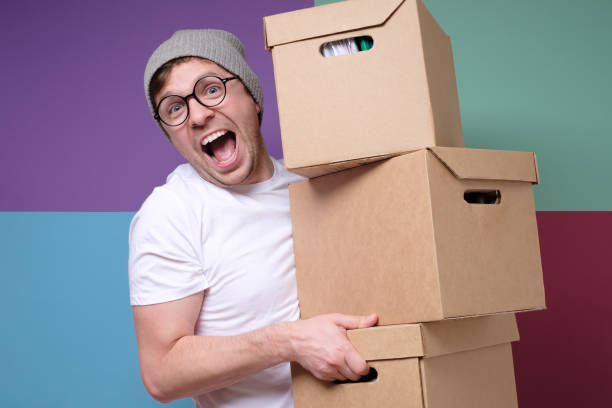 istock Young hipster man in hat and glasses carrying paper boxes isolated on colored background 1209685007