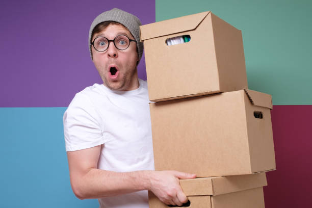 istock Young hipster man in hat and glasses carrying paper boxes isolated on colored background 1209685030
