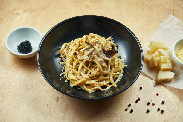 Classic, homemade pasta with black truffle, parmesan and mushrooms in black bowl. Traditional italian cuisine. stock photo