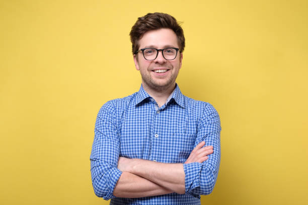 istock Handsome young man with folded hands smiling against yellow background 1209685882