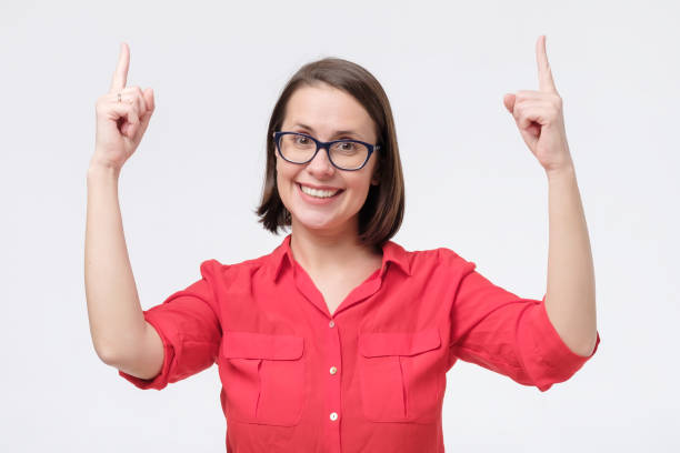 istock Woman in glasses smiling pointing up showing copy space. 1209687991