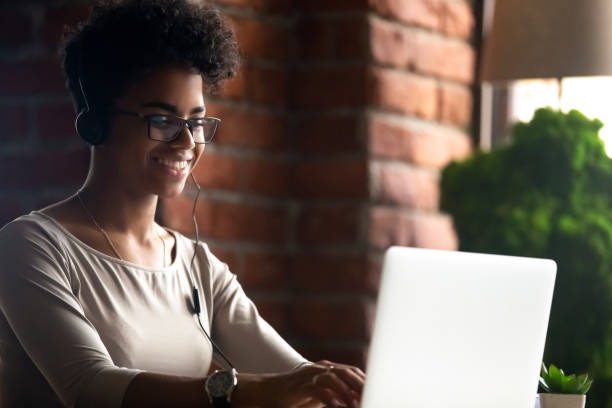 istock Smiling black girl in headset work at laptop online 1209689672