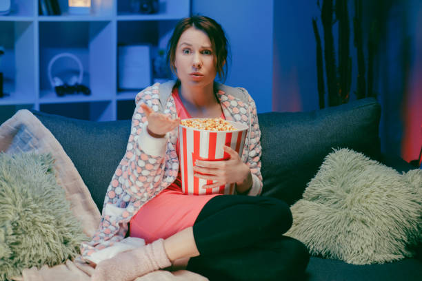 istock Woman sitting in living room sofa couch watching interesting program and pointing sharing with eating popcorn at night 1209693740