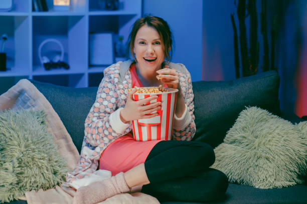 istock Woman sitting in living room sofa couch watching funny interesting program and pointing sharing with eating popcorn at night 1209693796