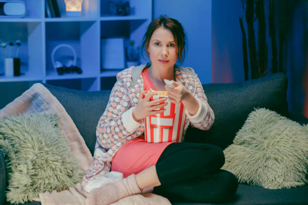 istock Happy woman sitting in living room sofa couch watching funny interesting program and pointing sharing with eating popcorn at night 1209693861