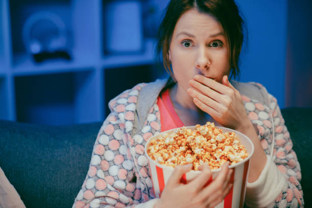 istock Woman with popcorn sitting on the sofa watching something scary while eating popcorn and being afraid 1209693991