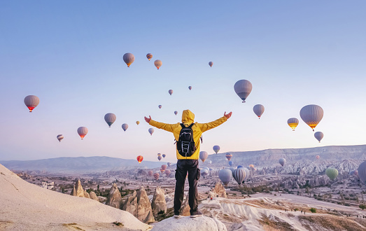 At dawn a tourist with a backpack on the background of soaring hot air balloons in Cappadocia, Turkey
