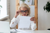 Middle-aged businesswoman lowered glasses reading letter feels shocked