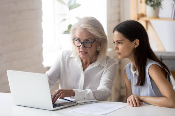 istock Mature woman mentor explain intern corporate application seated at desk 1209703827