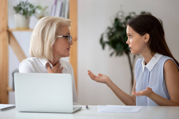 istock Middle-aged and millennial female colleagues arguing seated at workplace 1209703833