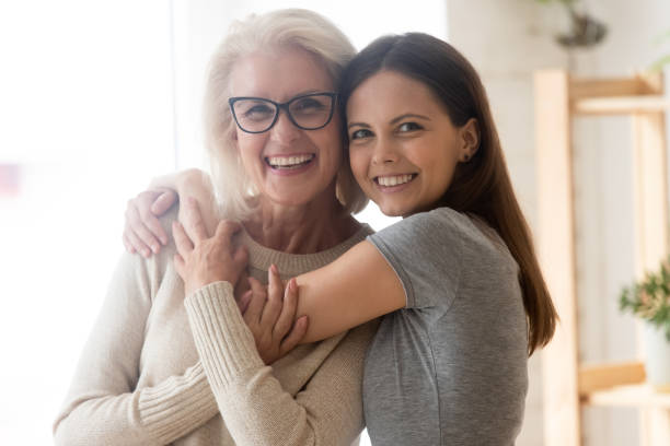mamá de mediana edad abraza y la hija adulta abrazando en el interior - senior women grandmother glasses senior adult fotografías e imágenes de stock