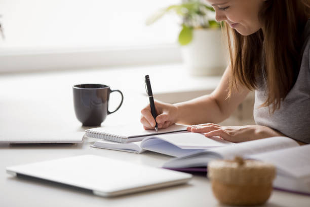 Student girl writing essay preparing for university entrance exams Close up of focused clever girl seated at desk writing essay preparing for university entrance exams, table fool of educational material. Personal development, assignment, student do homework concept exercise book stock pictures, royalty-free photos & images