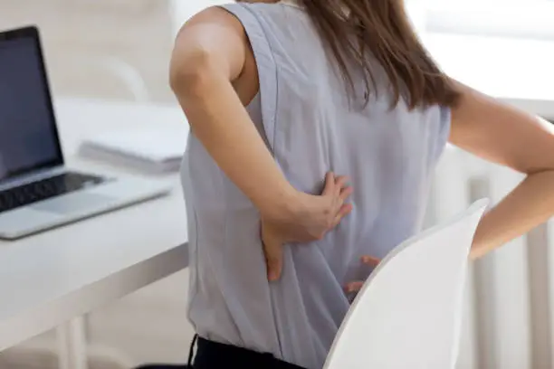 Rear close up view girl touch back feels unhealthy by uncomfortable office chair increase backpain. Sedentary work, wrong posture incorrect position, intervertebral disc, spinal joint damage concept