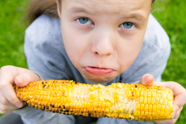 offended girl outdoors sits on grass and eats grilled corncob