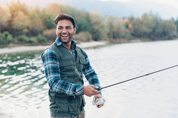 Fisherman enjoying his hobby Smiling young man with fishing rod by the river fishing industry stock pictures, royalty-free photos & images
