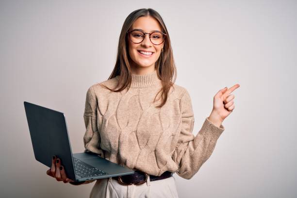 istock Young beautiful brunette woman working using laptop over isolated white background very happy pointing with hand and finger to the side 1209714023