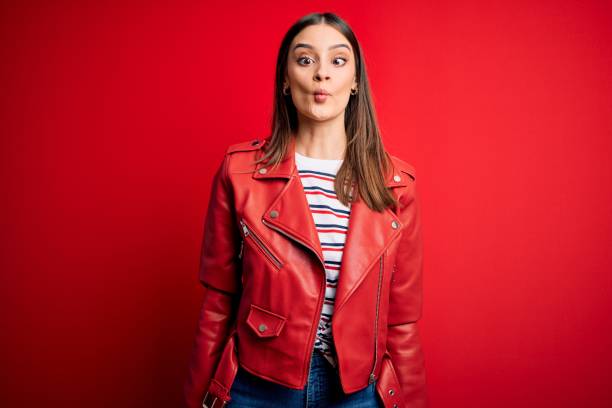 istock Young beautiful brunette woman wearing casual jacket standing over red background making fish face with lips, crazy and comical gesture. Funny expression. 1209714197