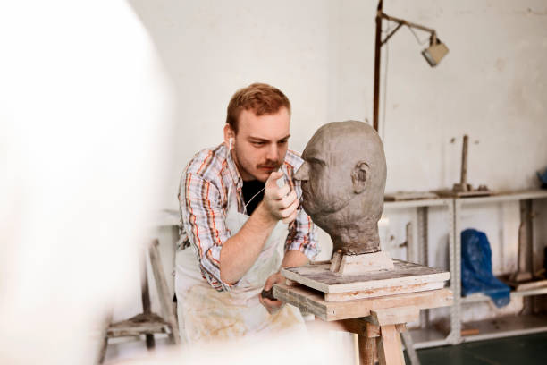istock Sculptor working on his clay head sculpture in studio wearing headphones 1209715139