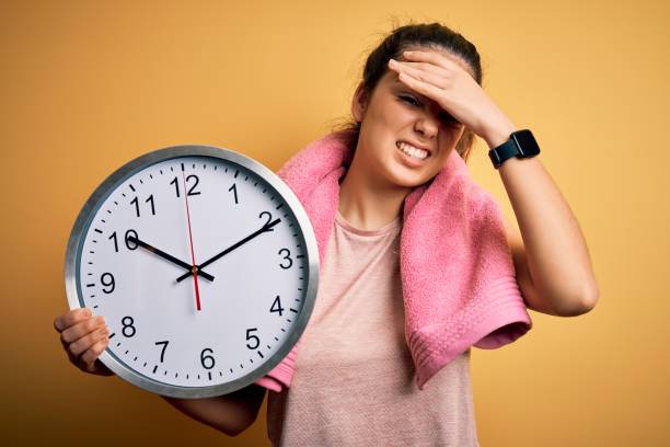 istock Young beautiful brunette sportswoman wearing towel doing countdown using big clock stressed with hand on head, shocked with shame and surprise face, angry and frustrated. Fear and upset for mistake. 1209715239