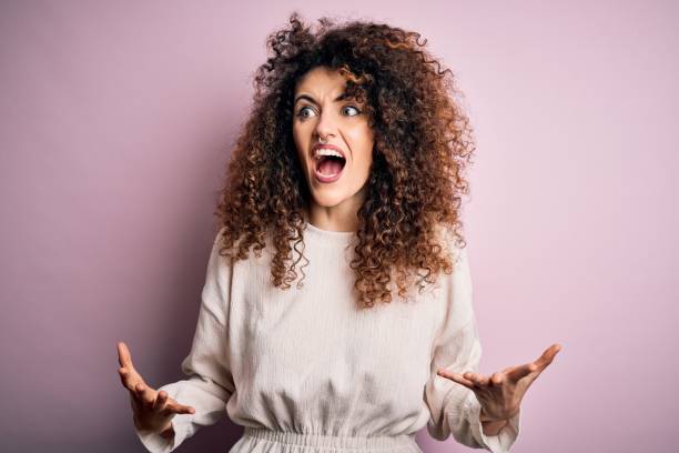 hermosa mujer con el pelo rizado y piercing usando suéter casual sobre fondo rosa loco gritos y gritos con expresión agresiva y los brazos levantados. concepto de frustración. - bizarre women portrait pierced fotografías e imágenes de stock