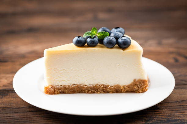 Plain New York Cheesecake Slice Topped With Blueberries And Mint Leaf Plain New York Cheesecake Slice Topped With Blueberries And Mint Leaf On White Plate Wooden Table Background. Tasty Slice Of Creamy Cake cream cake stock pictures, royalty-free photos & images