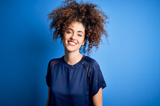 Young beautiful woman with curly hair and piercing wearing casual blue t-shirt with a happy and cool smile on face. Lucky person.