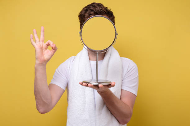 Anonym man looking at himself in the bathroom mirror showing ok sign. No face view. Yellow wall. Studio shot