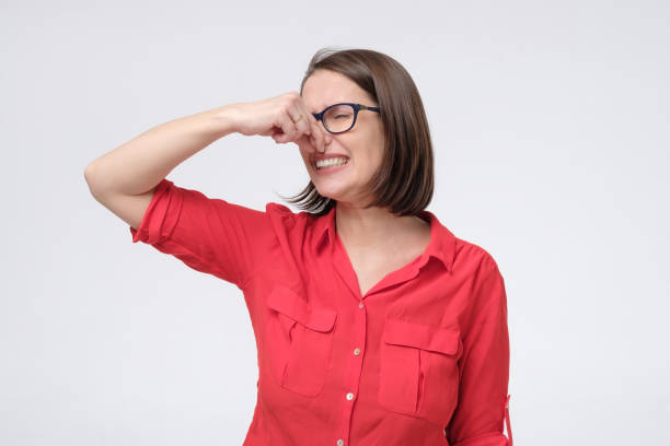 mature caucasian man in glasses and red shirt plugs close nose with fingers feels unpleasant scent - facial expression unpleasant smell shirt caucasian imagens e fotografias de stock