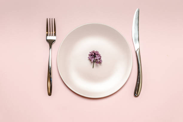 istock Lilac branch lies on a ceramic pink plate. Knife and fork on the table, flat lay style. Diet metaphor, nutrition plan concept 1209728544