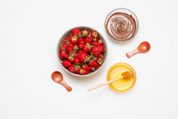 Top view of plate with strawberries, chocolate paste, honey and spoons