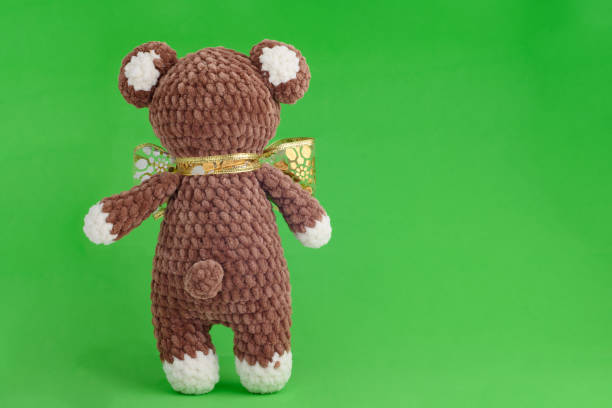 Children's knitted toy bear with bow on a green background
