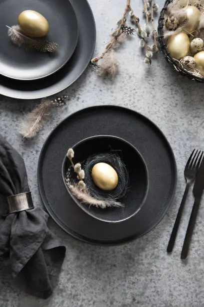 Easter table setting with black and golden decor on grey stone table. Top view. Vertical format.