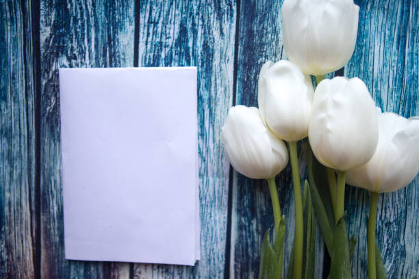 istock White tulips and white mockup blank on blue wooden background. Flat lay, top view, copy space 1209734282