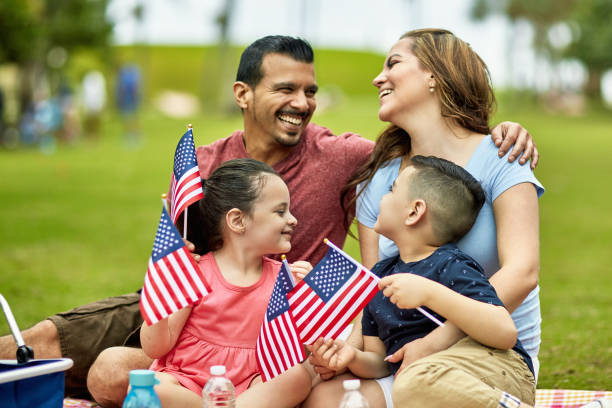 Hispanic Family Holding American Flags on Holiday Smiling Hispanic American family with pre-adolescent children holding American flags while celebrating holiday at Miami park with picnic. florida food stock pictures, royalty-free photos & images