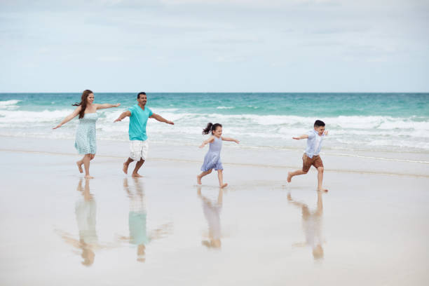 istock Hispanic Family Running Along Beach with Outstretched Arms 1209737110