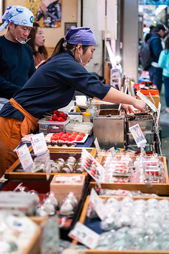 Kyoto, Japan - April 17, 2019: People serving at Nishiki market shops food vendor selling rice cake mochi sweets