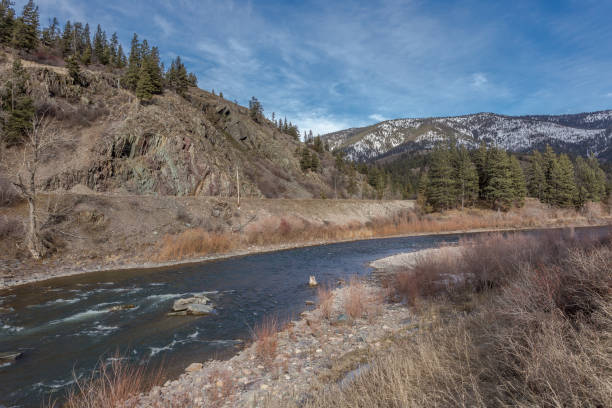 istock River curving through valley with rocky cliffs, tall evergreen trees and snow covered mountain range on clear day 1209742129