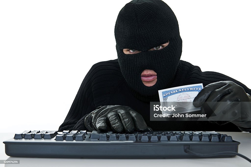 Burglar stealing an identity Burglar holding a Social Security card using computer to represent Identity theft  Con Man Stock Photo