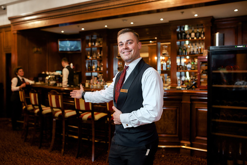 Portrait of smiling waiter welcoming guests in hotel restaurant. Horizontal shot