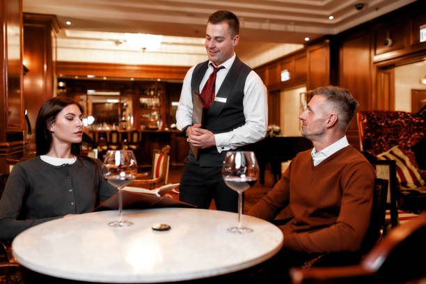 istock Service is our main purpose. Confident waiter giving menu to costumers. Couple having dinner in hotel restaurant 1209742649