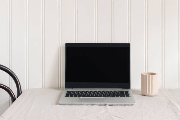 Feminine workspace composition with open laptop. Ceramic vase on beige linen tablecloth. White wooden wall background. Table arrangement. Business, entrepreneur concept. Blogger design.