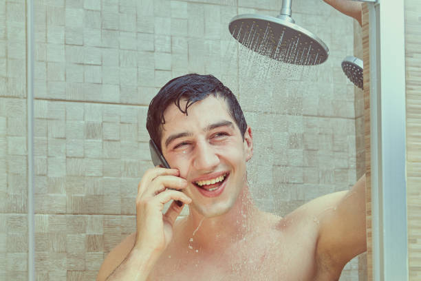 el hombre blanco sonriente usa el teléfono en un puesto de ducha. - diseño flux fotografías e imágenes de stock